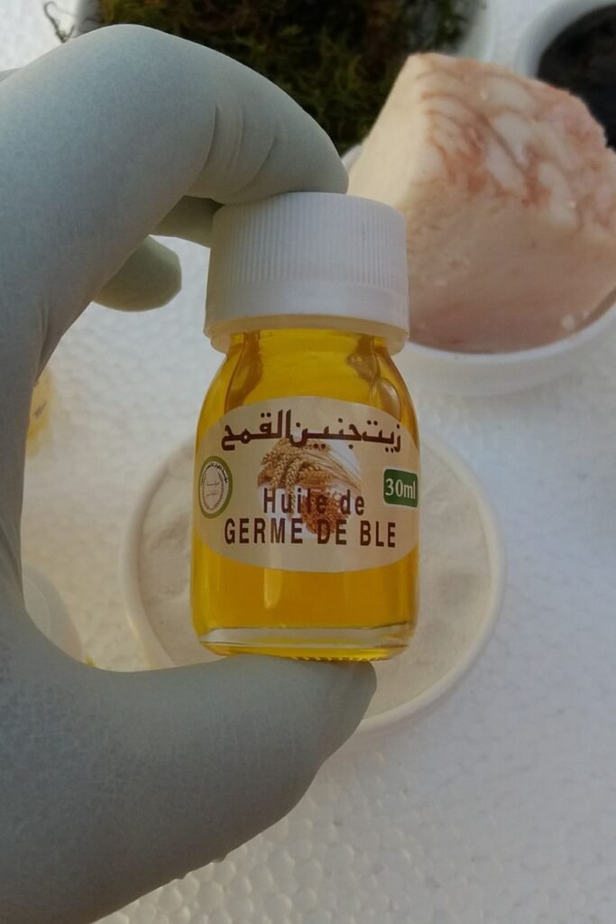 زيت جنين القمح الذهبي في وعاء أنيق بجانب سنابل القمح، يمثل المكونات الغنية بالفيتامينات في افضل كريم لتكبير الذكر مجرب لتعزيز الحيوية.