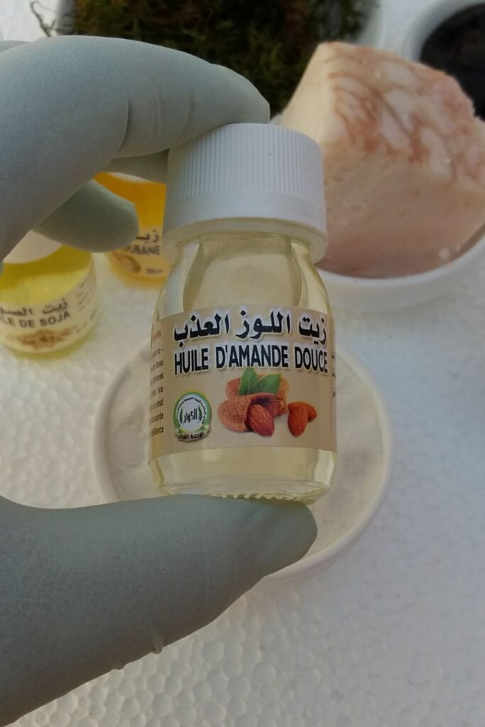زيت اللوز الحلو ينساب بنعومة بجانب أزهار اللوز، مما يصور الترطيب والمرونة التي يمنحها افضل كريم لتكبير الذكر مجرب.